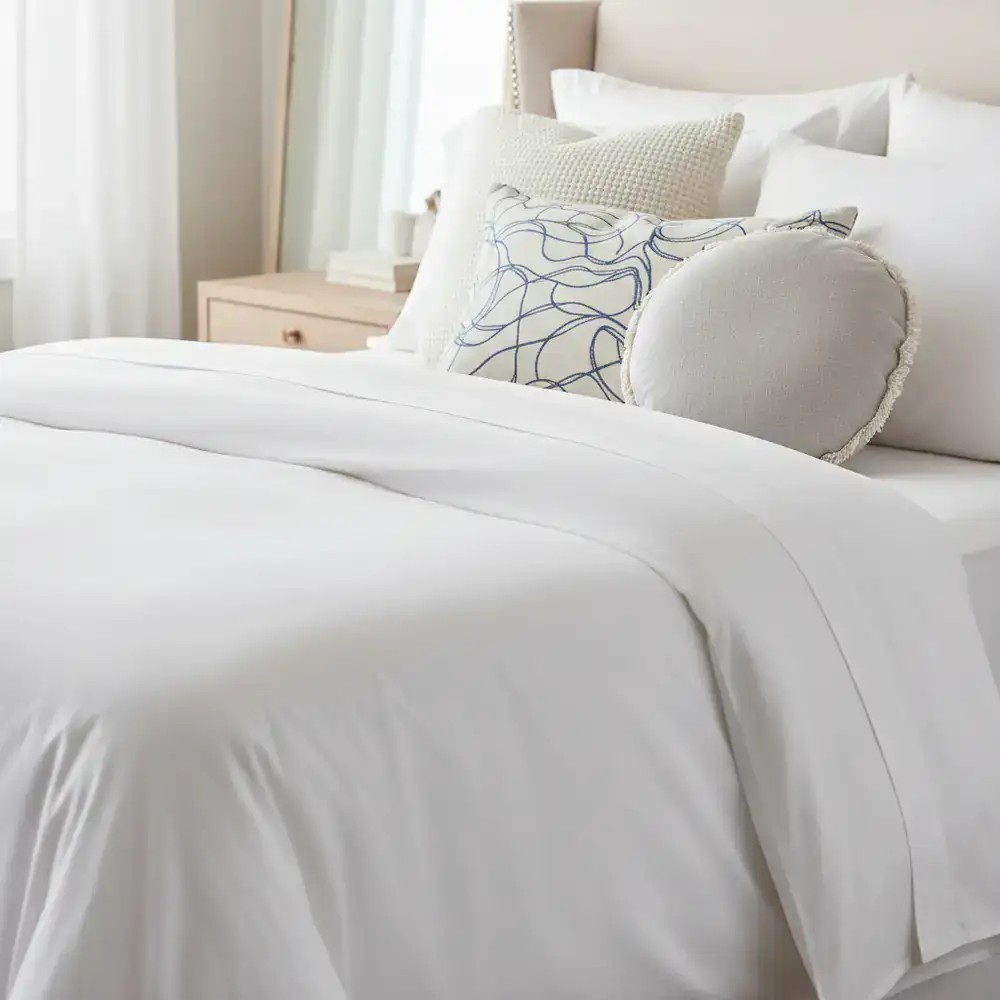 Detail shot of a freshly made bed with crisp white linens and accent pillows